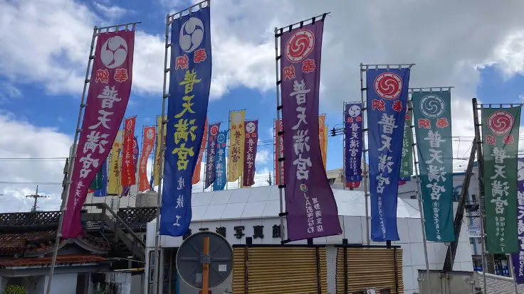 普天間交差点そばの普天満宮入口。のぼり旗が並び、鳥居横の細い道から境内駐車場へ上がれる。