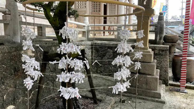 普天満宮のおみくじ掛け。初穂料100円で引けるおみくじが結ばれ、白い紙が風に揺れている。