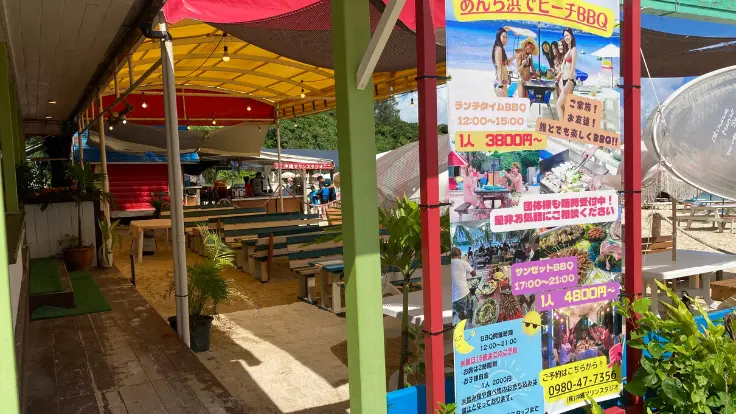 アンチ浜の白い砂浜で、パラソルの下でのんびり過ごす様子。そばにはBBQスペースや軽食販売コーナーも完備。