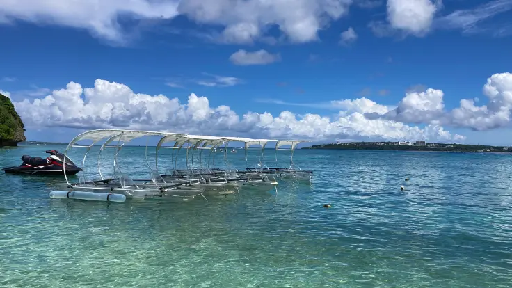 屋根付きのグラスカヤックでアンチ浜の海を楽しむ様子。透明な船底から熱帯魚が見える人気体験。