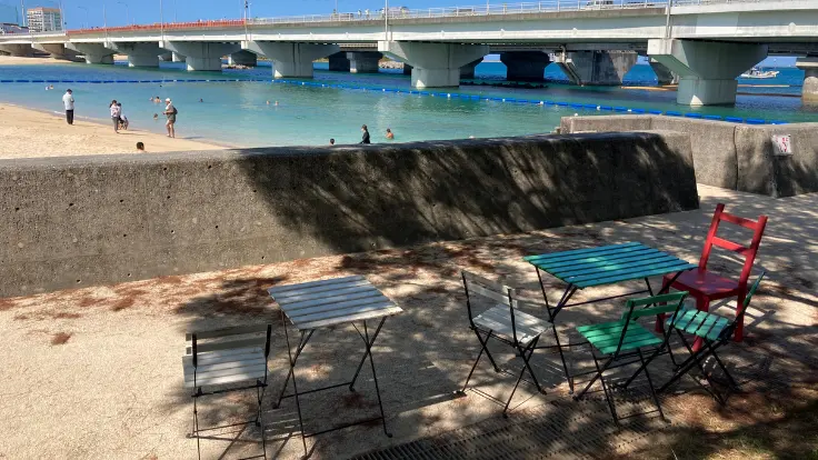 波の上ビーチのテラス席。青い海を目の前に、ドリンクや軽食を楽しみながらゆったり過ごす人々。