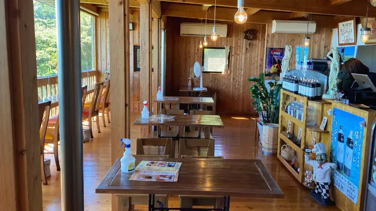 南城市の絶景ピザカフェ『ミモザの木』の店内。木の温もりあるインテリアと大きな窓から差し込む光が心地よい空間をつくり出している。