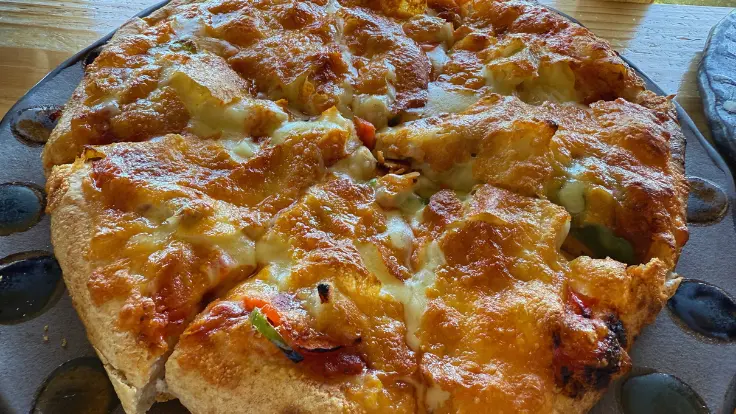 南城市の絶景カフェ『ミモザの木』名物、小谷ピザ。沖縄の伝統食スーチカー(塩漬け豚肉)がトッピングされ、モチモチ生地ととろけるチーズが相性抜群。