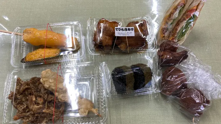 おんなの駅のローカルグルメ勢ぞろい。ポークたまご、沖縄てんぷら、もずく惣菜、サーターアンダギーなどが並ぶ。