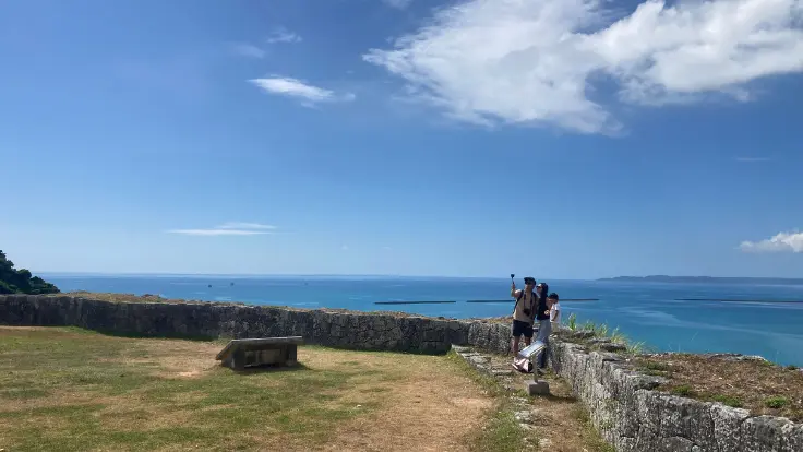 勝連城跡の高台から海を背景に写真を撮る観光客。絶景を楽しめる人気フォトスポット。