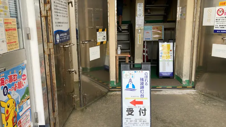 白い残波岬灯台の入口。晴れた空の下、階段とフェンスが続くシンプルな風景。