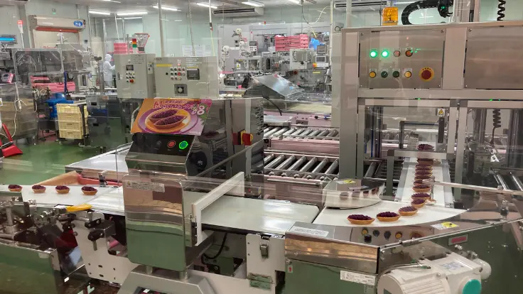 お菓子御殿 読谷本店の工場見学エリア。ガラス越しに紅いもタルトの製造工程を見ることができ、観光客が興味深そうに見学している。