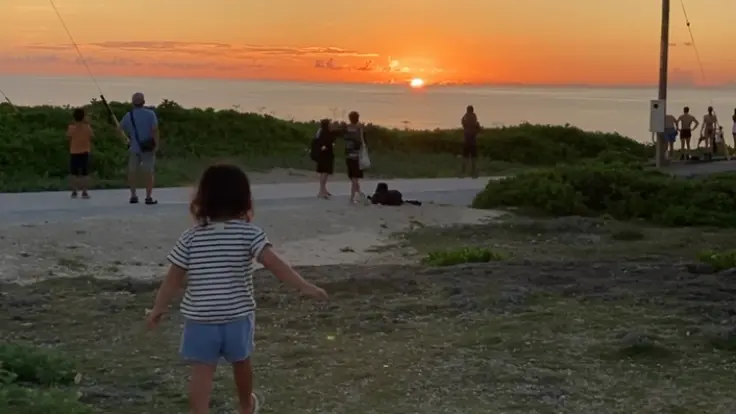 残波岬の灯台下で夕日を見つめる人々。観光客だけでなく地元の人々も訪れる、人気の夕日スポット。