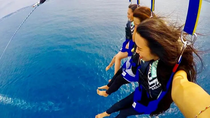 沖縄の海の上で、女性が空中で楽しそうにパラセーリングを体験している様子