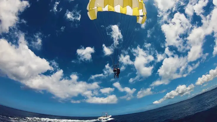 沖縄の海でパラセーリング船が沖へ向かう風景。エリアによって見える海の色や景色が変わるイメージ