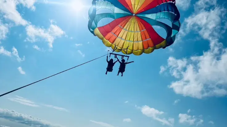 沖縄の快晴の日にパラセーリングを楽しんでいる様子。青い空と海がくっきり広がる絶景シーン