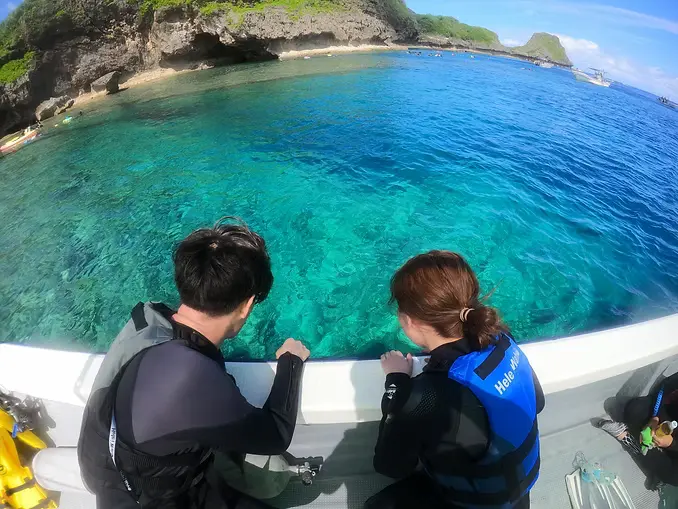 琉球石灰岩のダイナミックな岩場のそばを泳ぐダイバーと、透明度の高い真栄田の海中景色