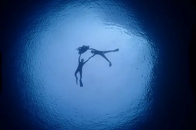 太陽の光が差し込む水中で、カメラに向かって手を振る体験ダイビング参加者の笑顔シーン